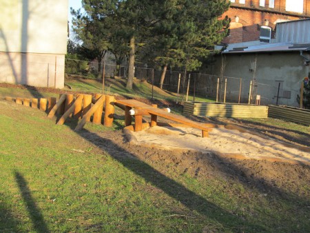 Pískoviště s balančními prvky, v pozadí záhony pro výsadbu rostlin dětmi